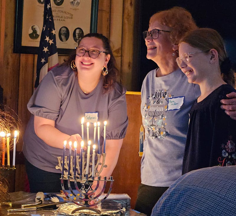 three ladies lighting a menorah